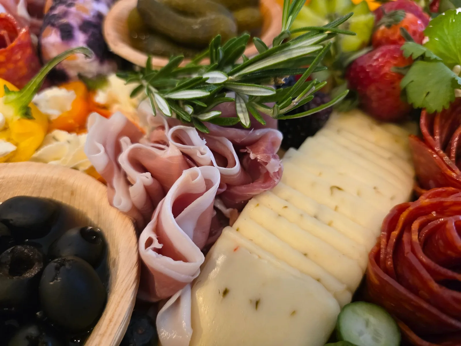 A tightly framed appetizer board displays folded pink cured meats, pale herb-flecked cheese, and round red salami slices.