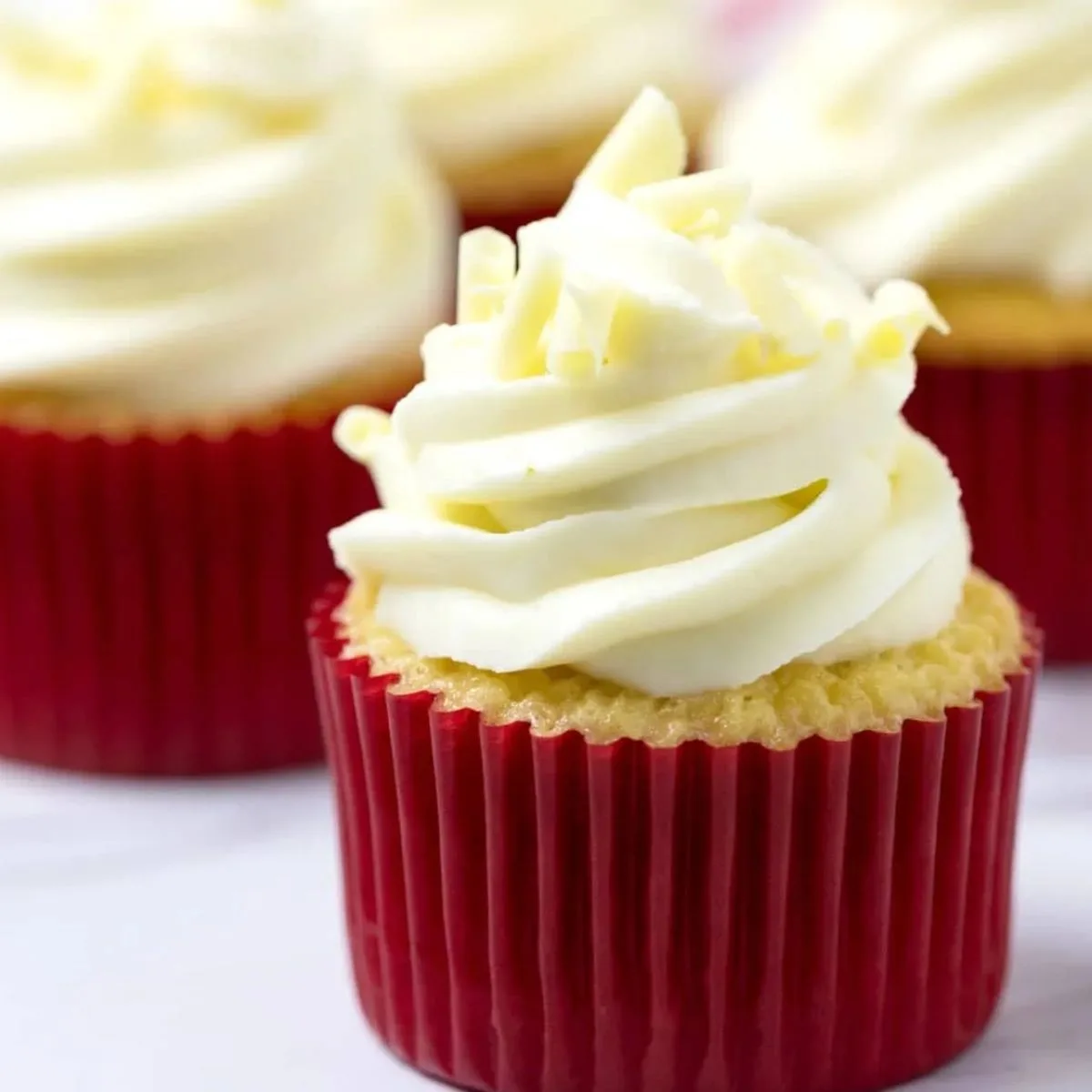 Cupcakes with swirled white buttercream frosting in red paper liners.