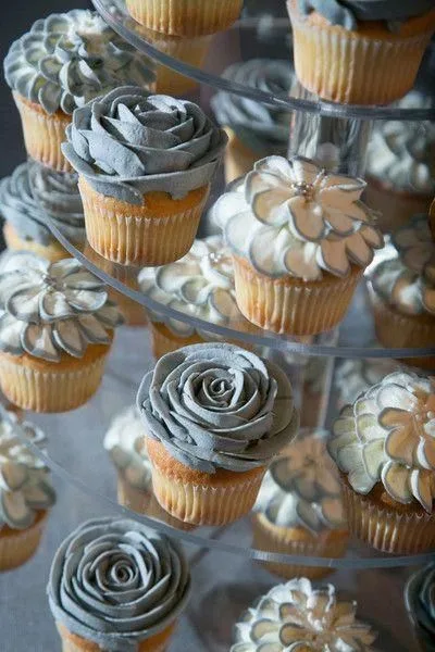 Tiered display of vanilla cupcakes topped with silver frosting piped into rose and daisy shapes with metallic accents.