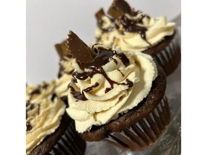 Cupcakes with swirled cream-colored frosting, drizzled with chocolate sauce, and topped with chunks of chocolate pieces in paper liners.