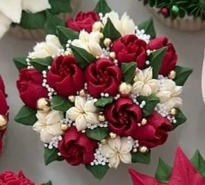 Cupcakes decorated to resemble a bouquet with red roses, white blossoms, green leaves, and gold pearl accents arranged in a circular display.